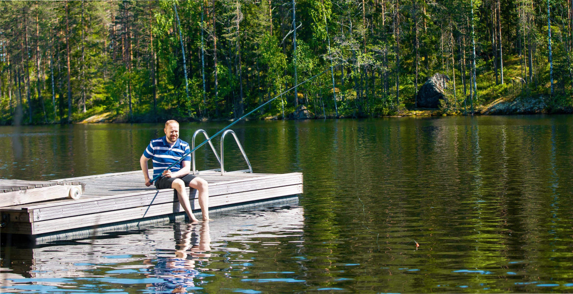 Mies istuu laiturilla ja onkii. Kuvituskuva.